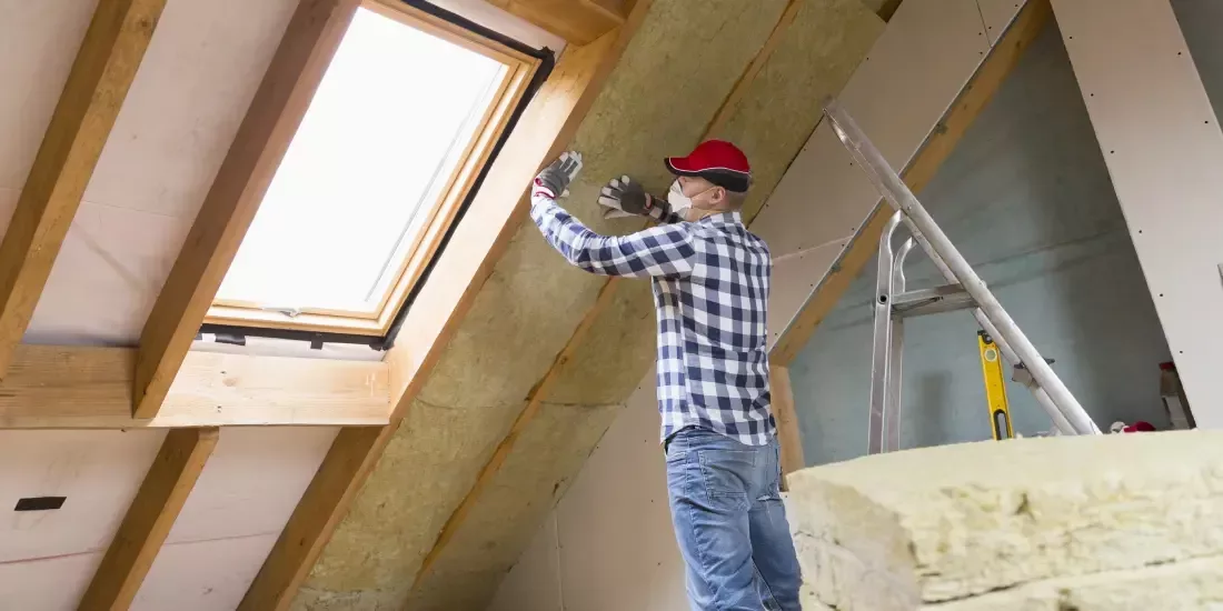 A professional installs sheet insulation to the rafters of loft